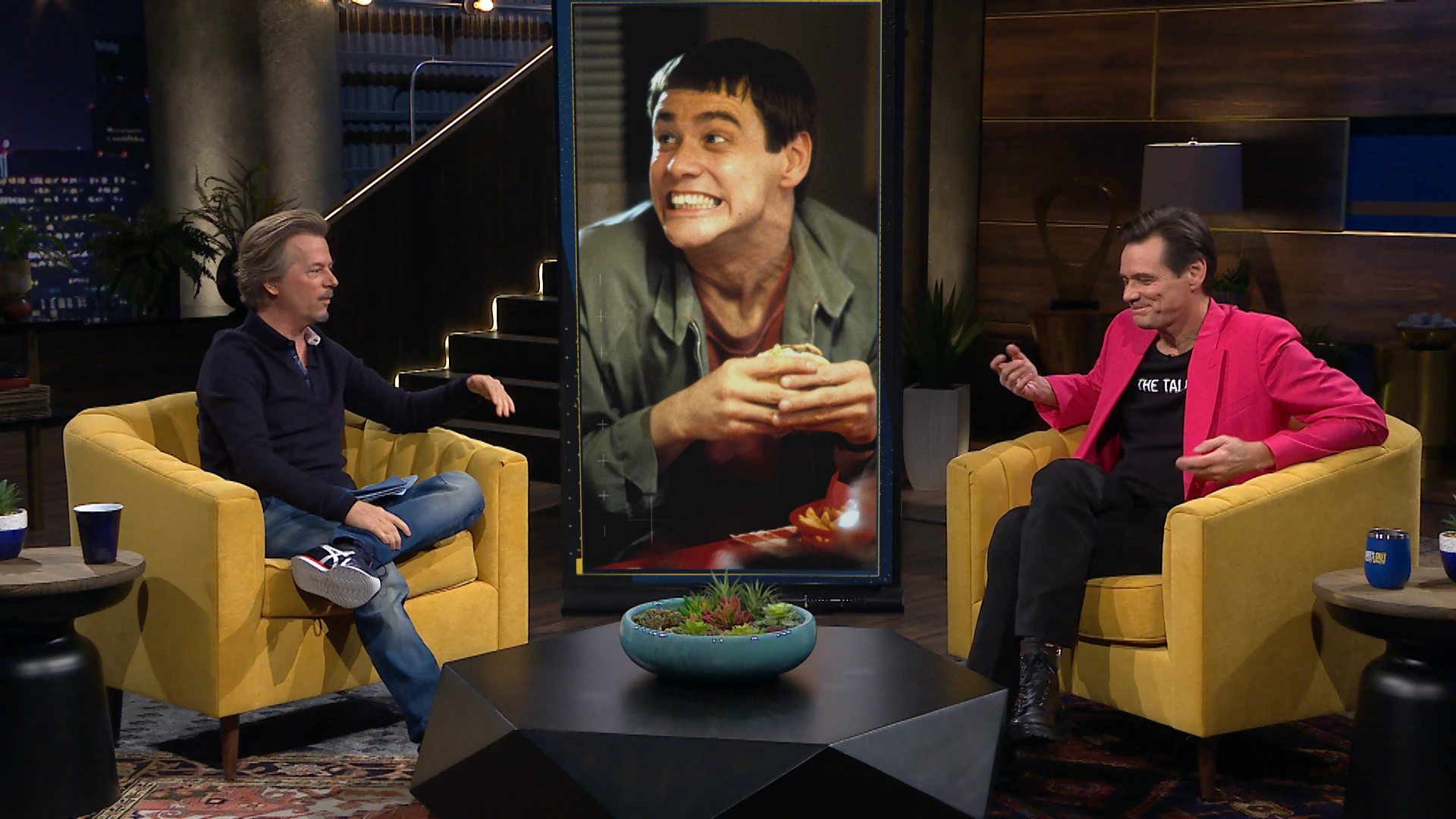 David Spade on the Lights Out set beside a Jim Carrey image.