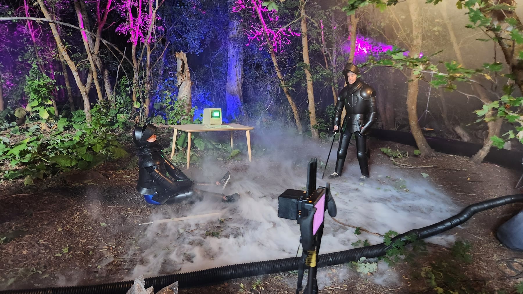 Behind-the-scenes view of perimeter tubing, practical ground fog, Macintosh, performers and lighting across the forest set.